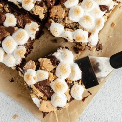 A spatula lifts a s'mores brownie away from the other brownies on a piece of parchment paper.