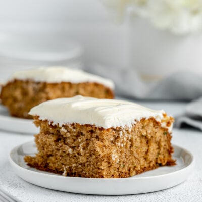 Two slices of zucchini cake on white plates next to a fork.