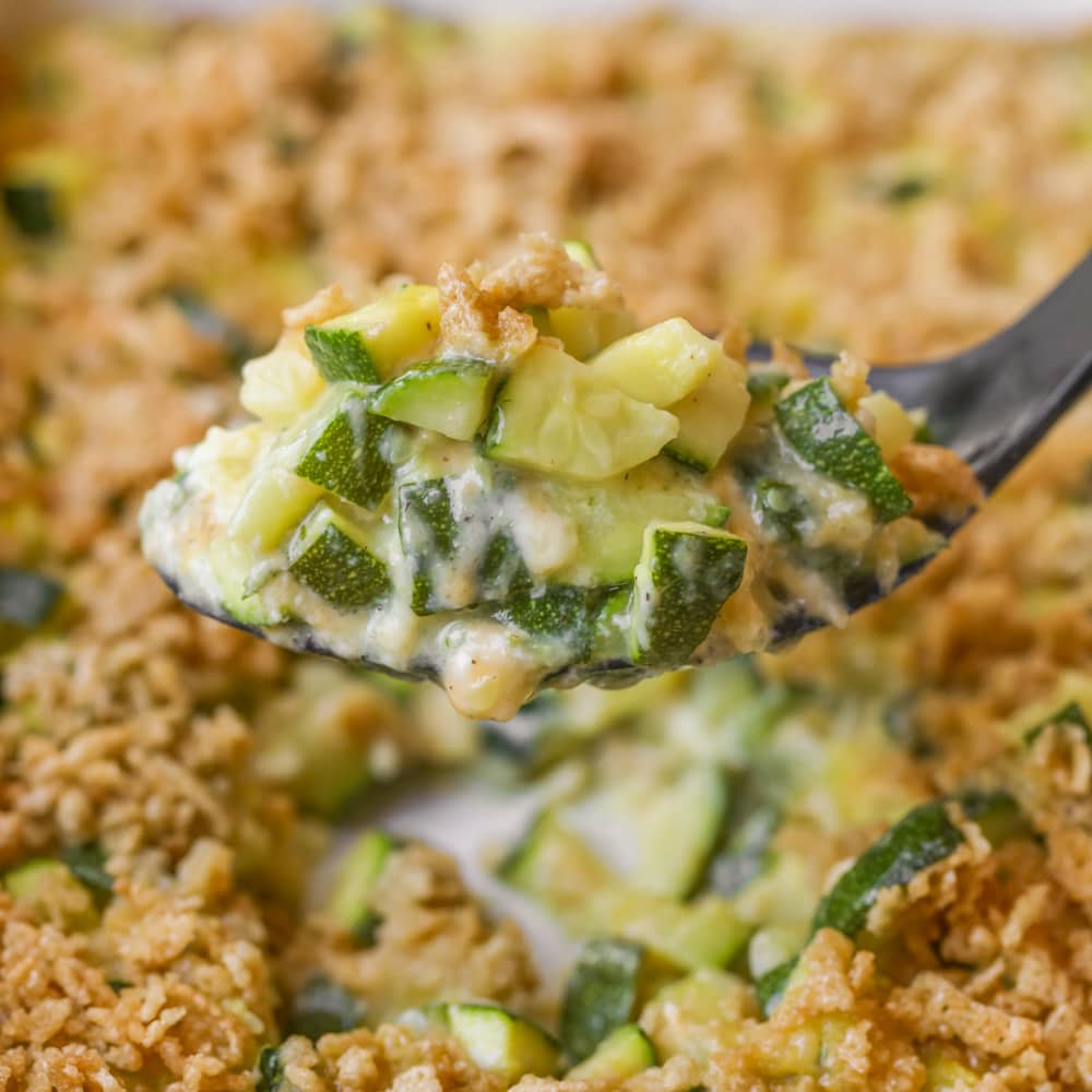 Vegetable side dishes - cheesy zucchini casserole being scooped from a baking dish.