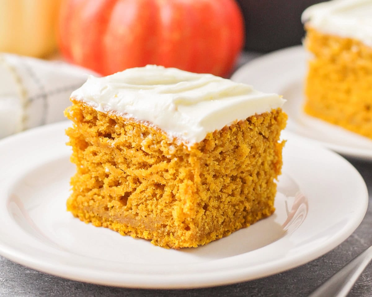 Easy pumpkin cake recipe with cream cheese frosting on white plate.
