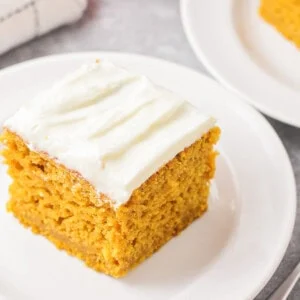 Pumpkin cake with cream cheese frosting on white plate.