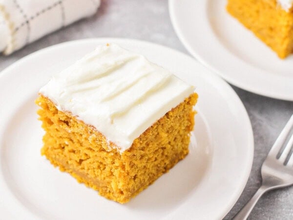 Pumpkin cake with cream cheese frosting on white plate.