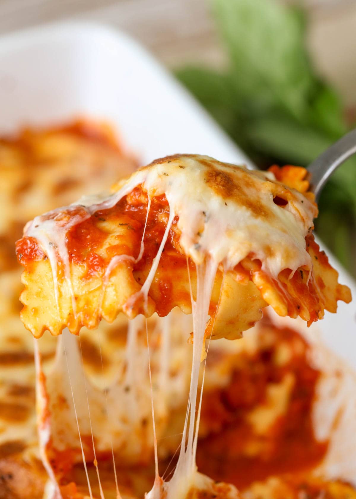 A spoonful of baked ravioli casserole being scooped from a baking dish.