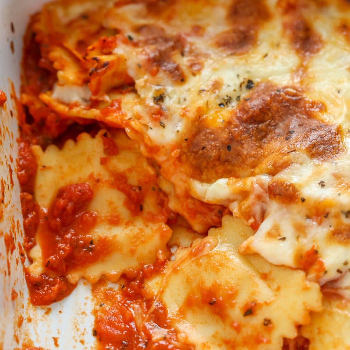 3 Ingredient Recipes - Close up of cheesy baked ravioli in a white baking dish.