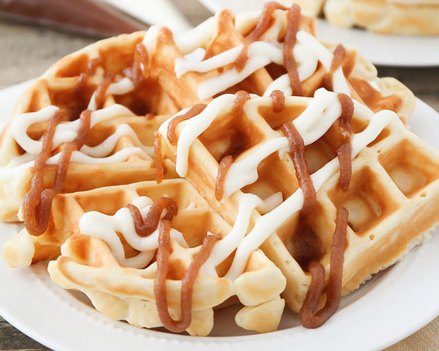 Cinnamon roll waffles drizzled with icing on a white plate. 