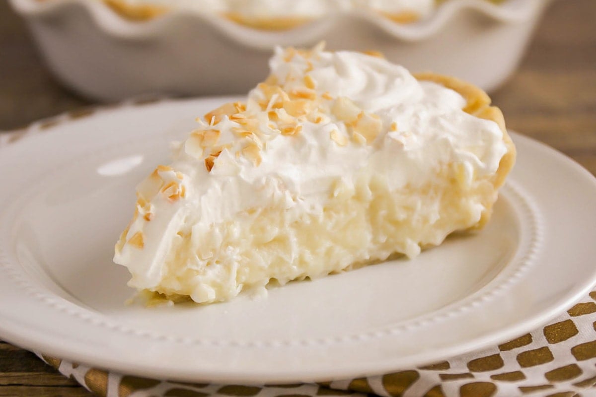 A slice of coconut cream pie on a white plate