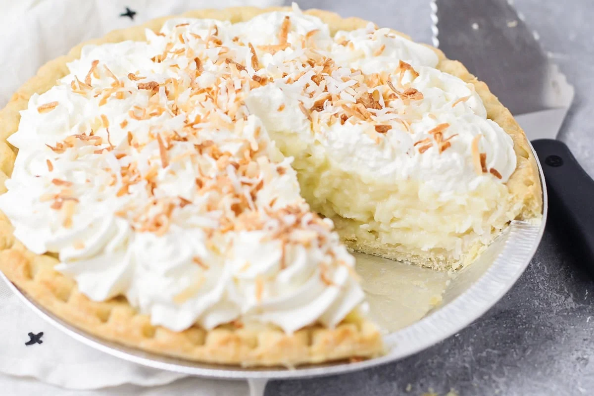 Old-fashioned coconut cream pie is filled with a thick and creamy homemade custard that whips up in only 15 minutes - it's hard to resist! Coconut cream pie recipe with slice taken out of it.