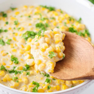 Creamed corn recipe being spooned out of baking dish.