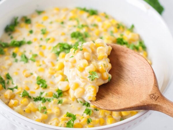 Creamed corn recipe being spooned out of baking dish.