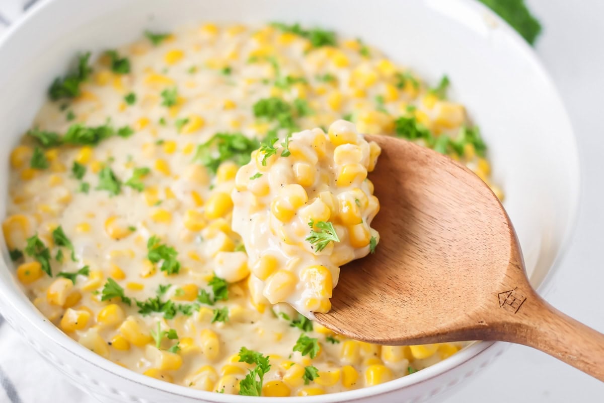 Creamed corn recipe being spooned out of baking dish.