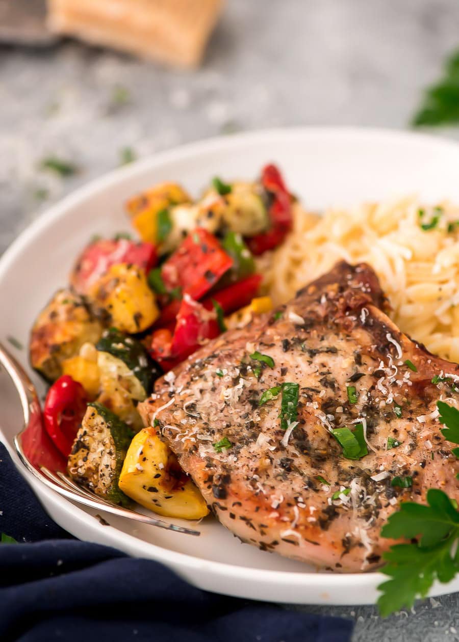 Closeup of a baked Italian pork chop on a plate with vegetables and pasta