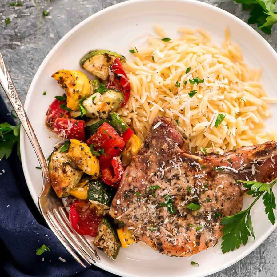 An Italian seasoned pork chop on a plate with orzo pasta and veggies