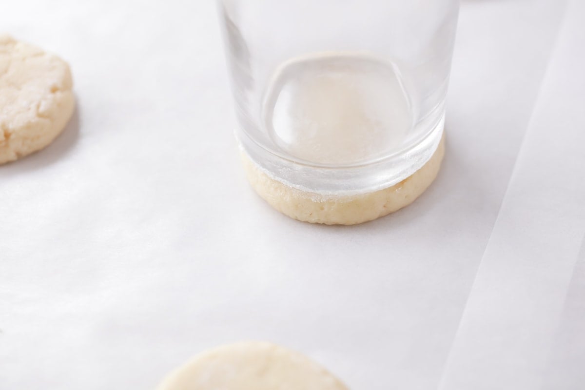 Pressing cookie dough balls flat with a glass cup.