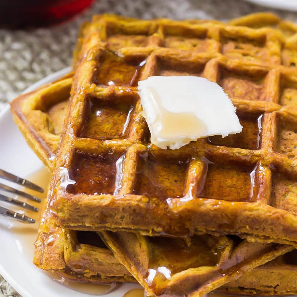 A stack of pumpkin waffles topped with butter and syrup