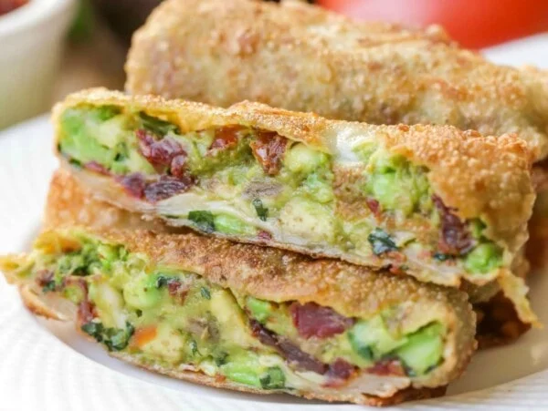 Homemade avocado egg rolls stacked on a white plate.