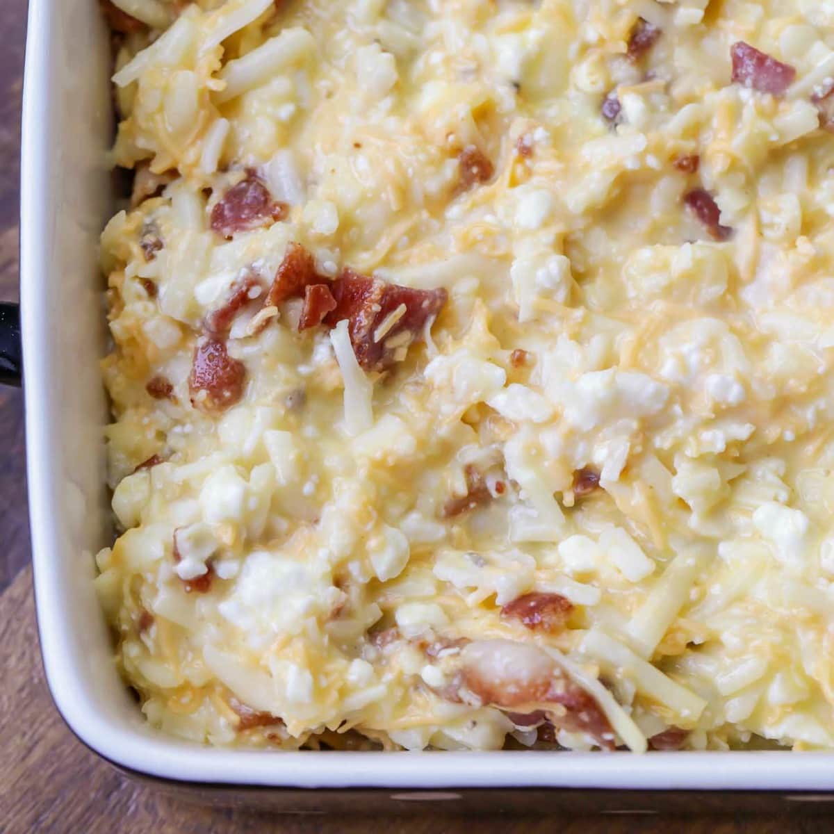 Close up of uncooked hashbrowns and cheesy sauce in a baking dish.