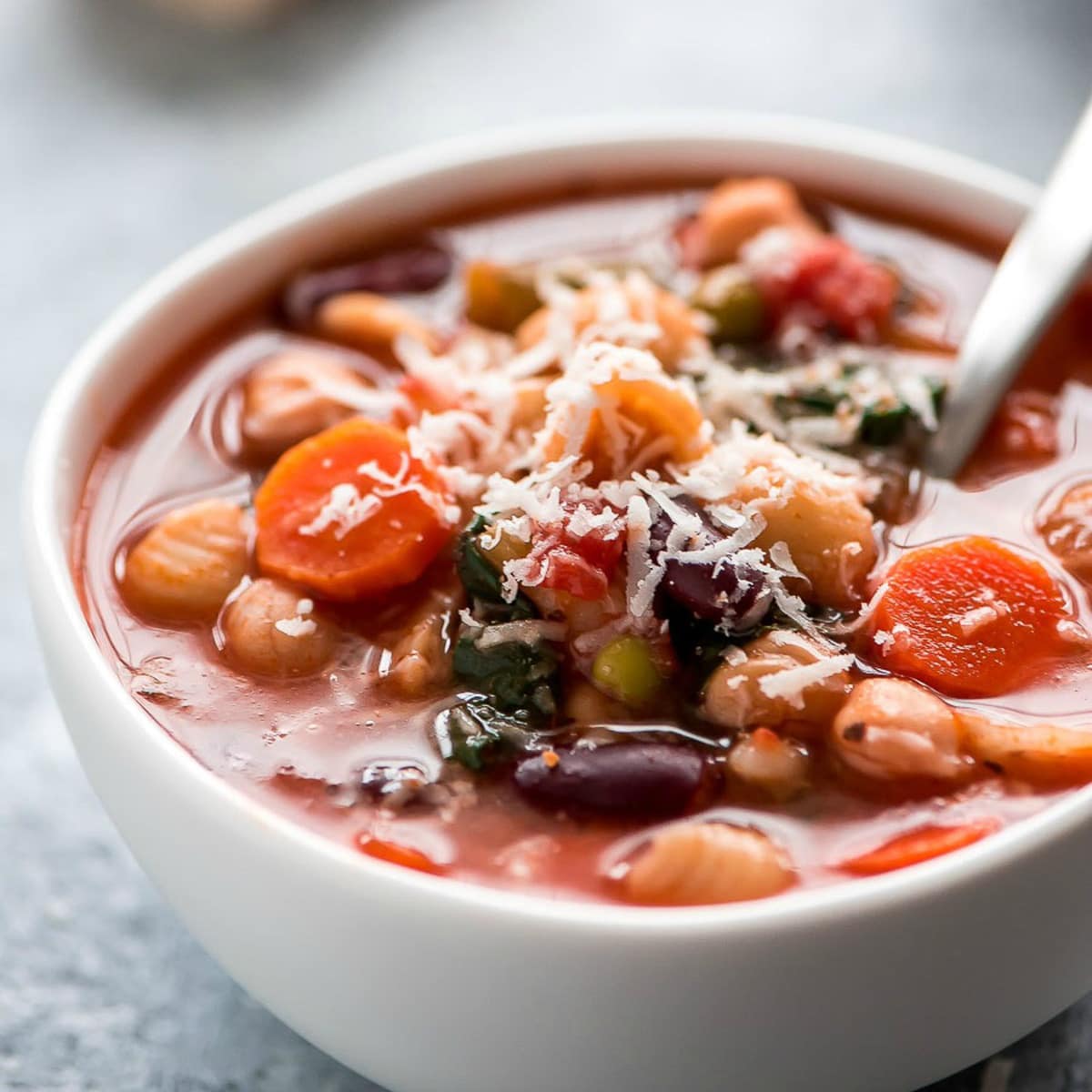Healthy Soup Recipes - Minestrone soup in a white bowl topped with grated Parmesan cheese.