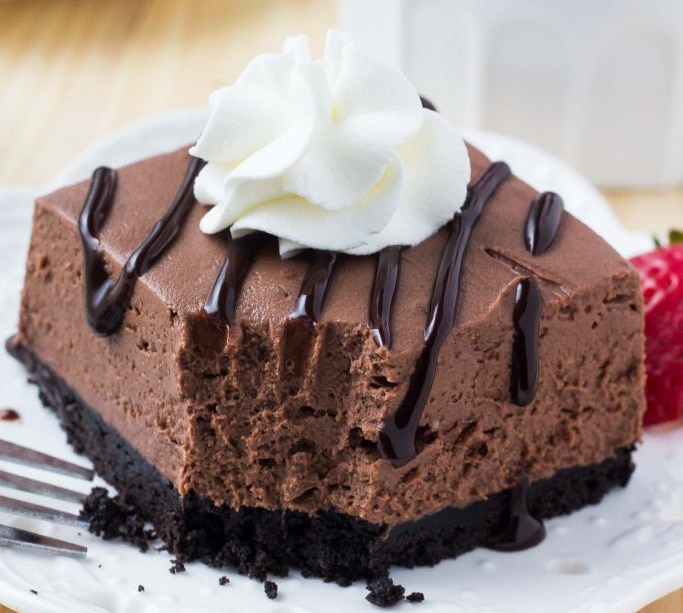 Valentine's Day Desserts - no bake chocolate cheesecake drizzled with chocolate and topped with whipped cream on a white plate. 