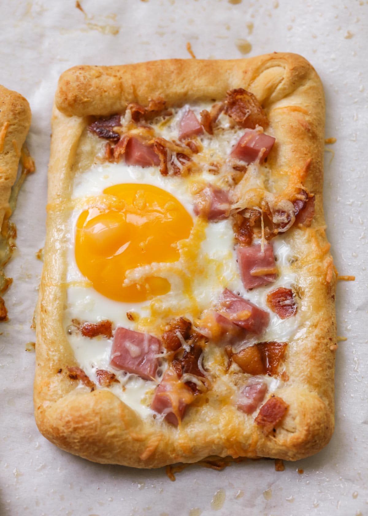 Crescent roll breakfast hand pies topped with egg and ham on a baking pan.