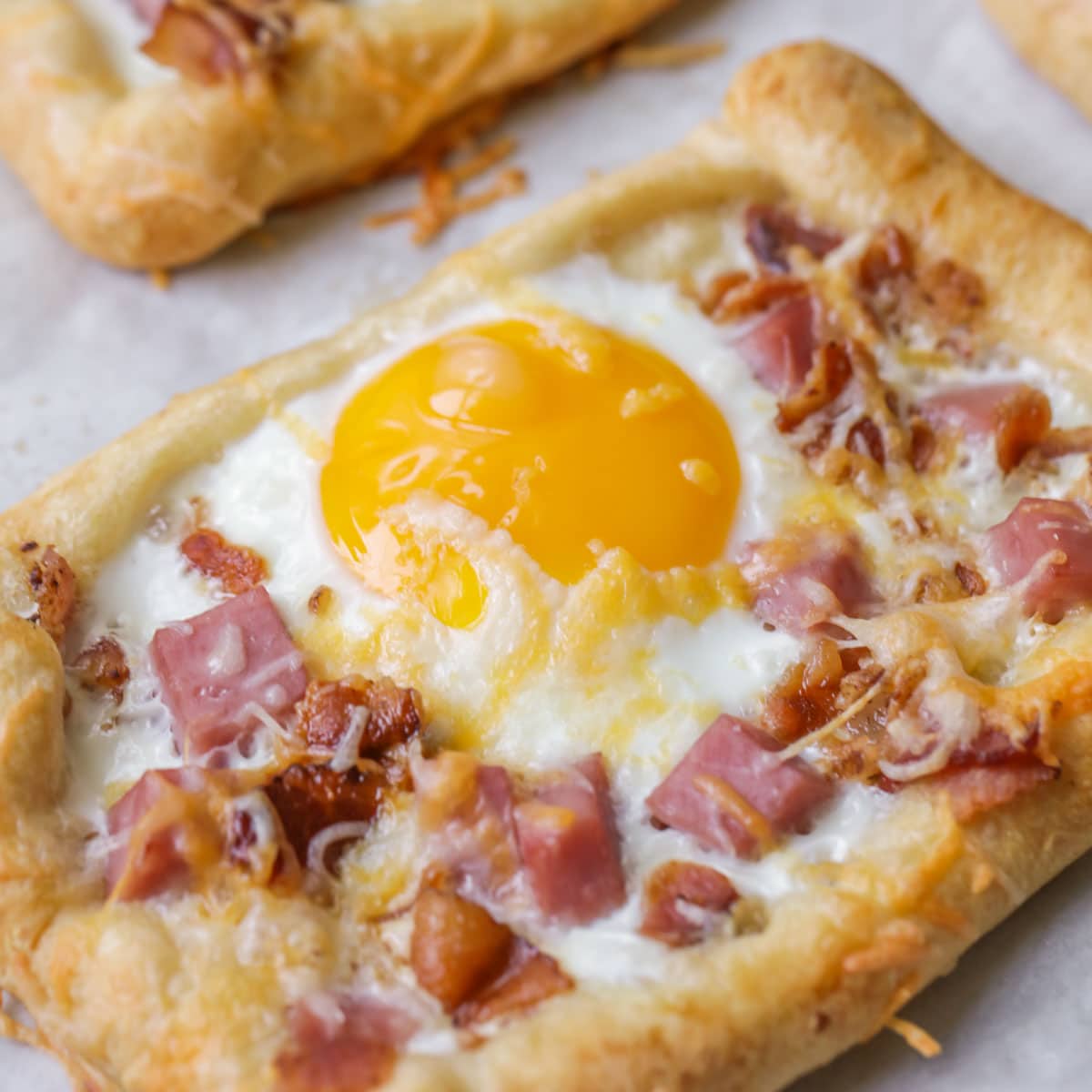 Breakfast hand pies topped with ham and eggs on a baking sheet.