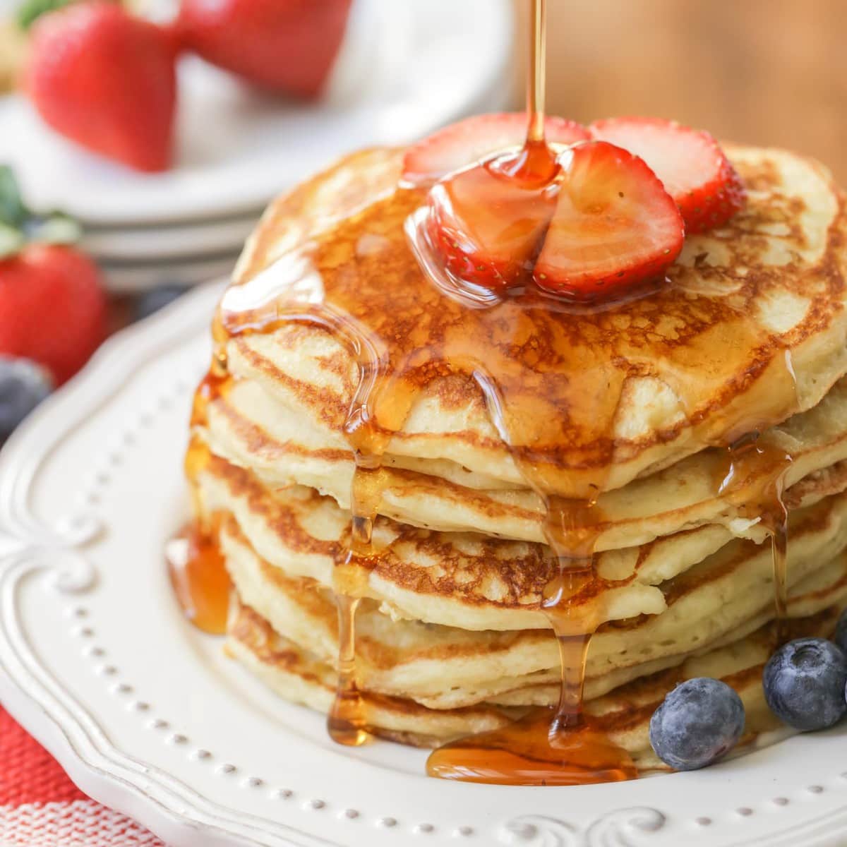 Buttermilk Pancakes stacked on a white plate covered in syrup.