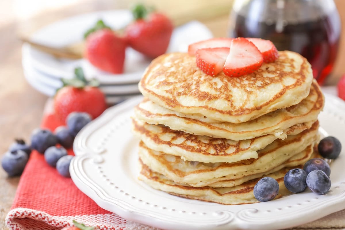 A stack of buttermilk pancakes on a white plate served with blueberries and strawberries.