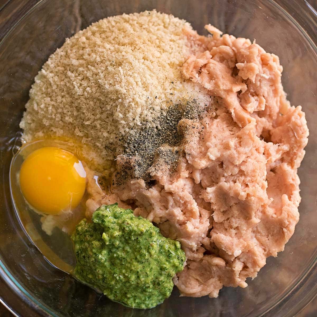 Pesto meatball ingredients in a glass mixing bowl