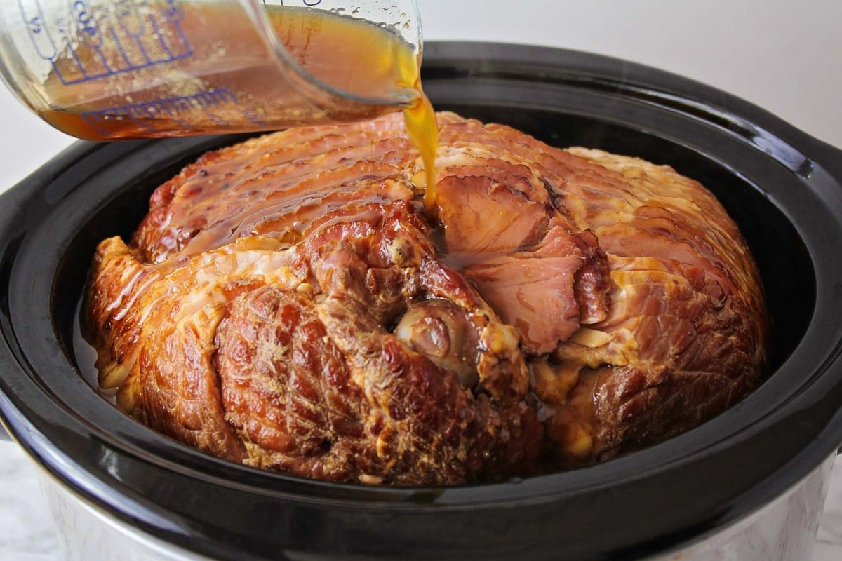 Honey glaze being poured over ham in crock pot.