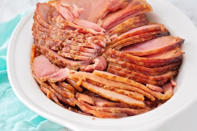 Honey glazed ham sliced and placed on white platter.