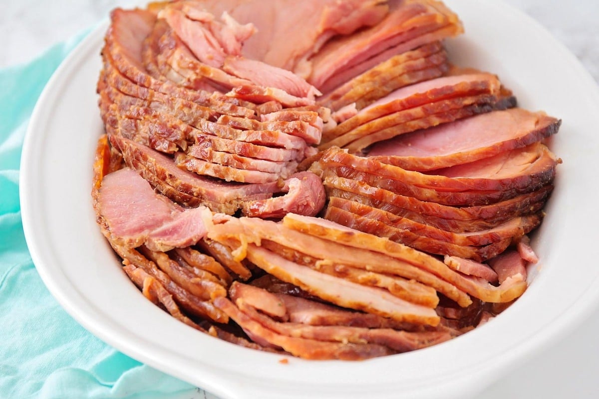 Thanksgiving dinner ideas - sliced honey glazed ham in a white serving bowl.