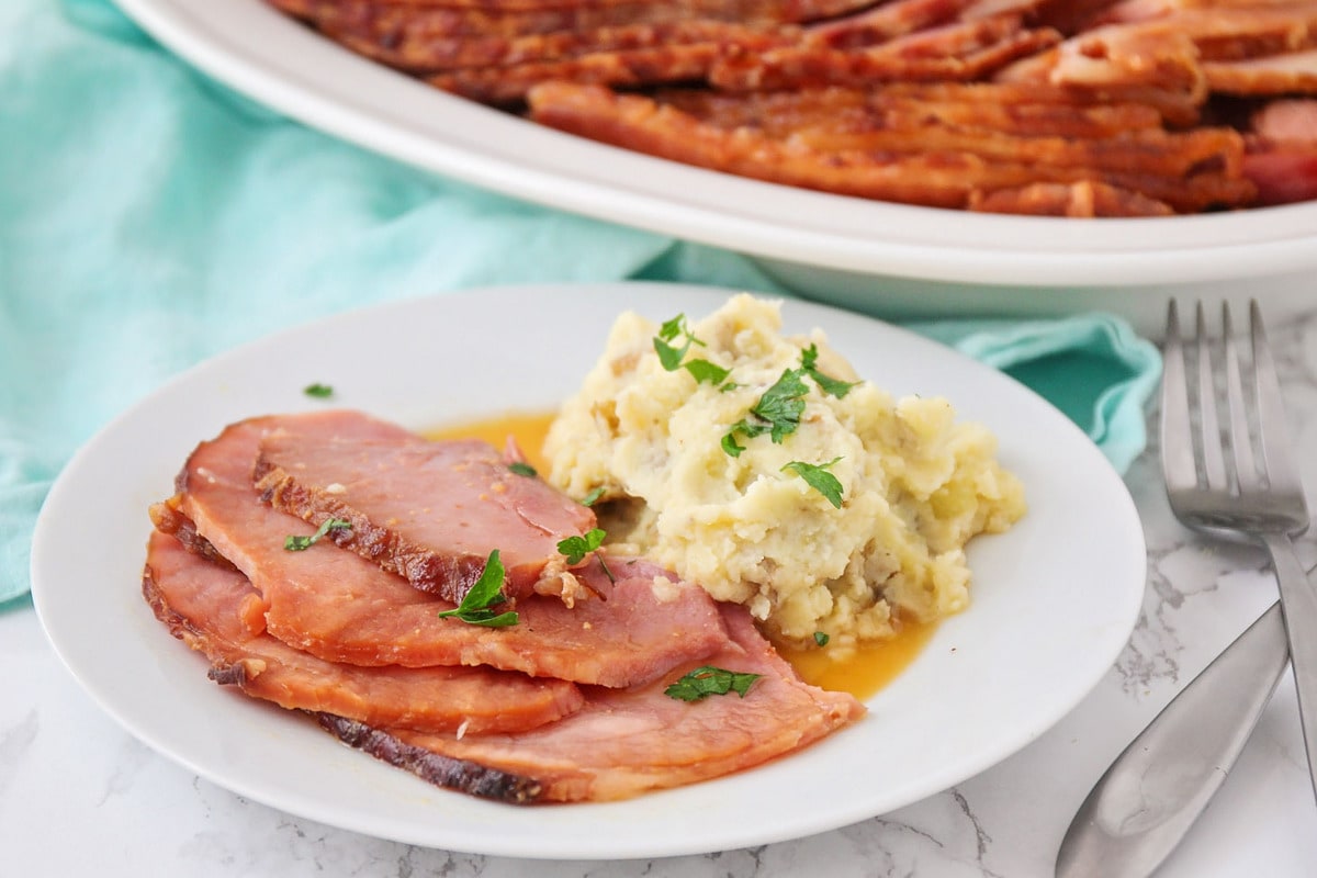 Sliced ham served on a plate with a side of potatoes.