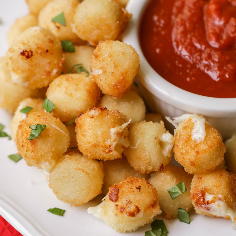 Fried mozzarella bites on a platter with marinara sauce.