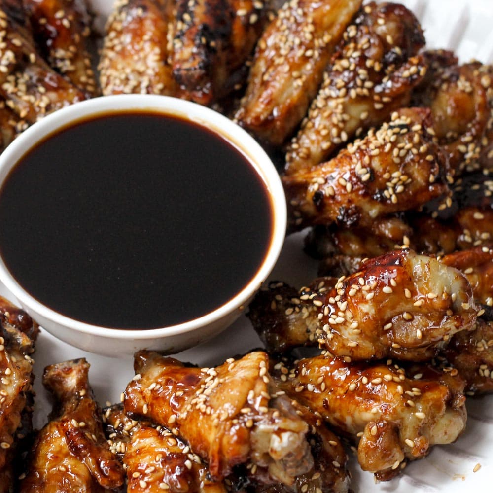 Super Bowl Appetizers - Teriyaki Chicken wings with a side of teriyaki sauce on a white plate. 
