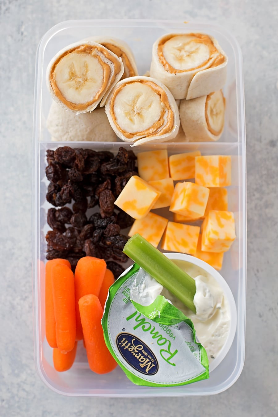 Healthy lunch box idea with peanut butter bananas, cheese, raisins, and carrots