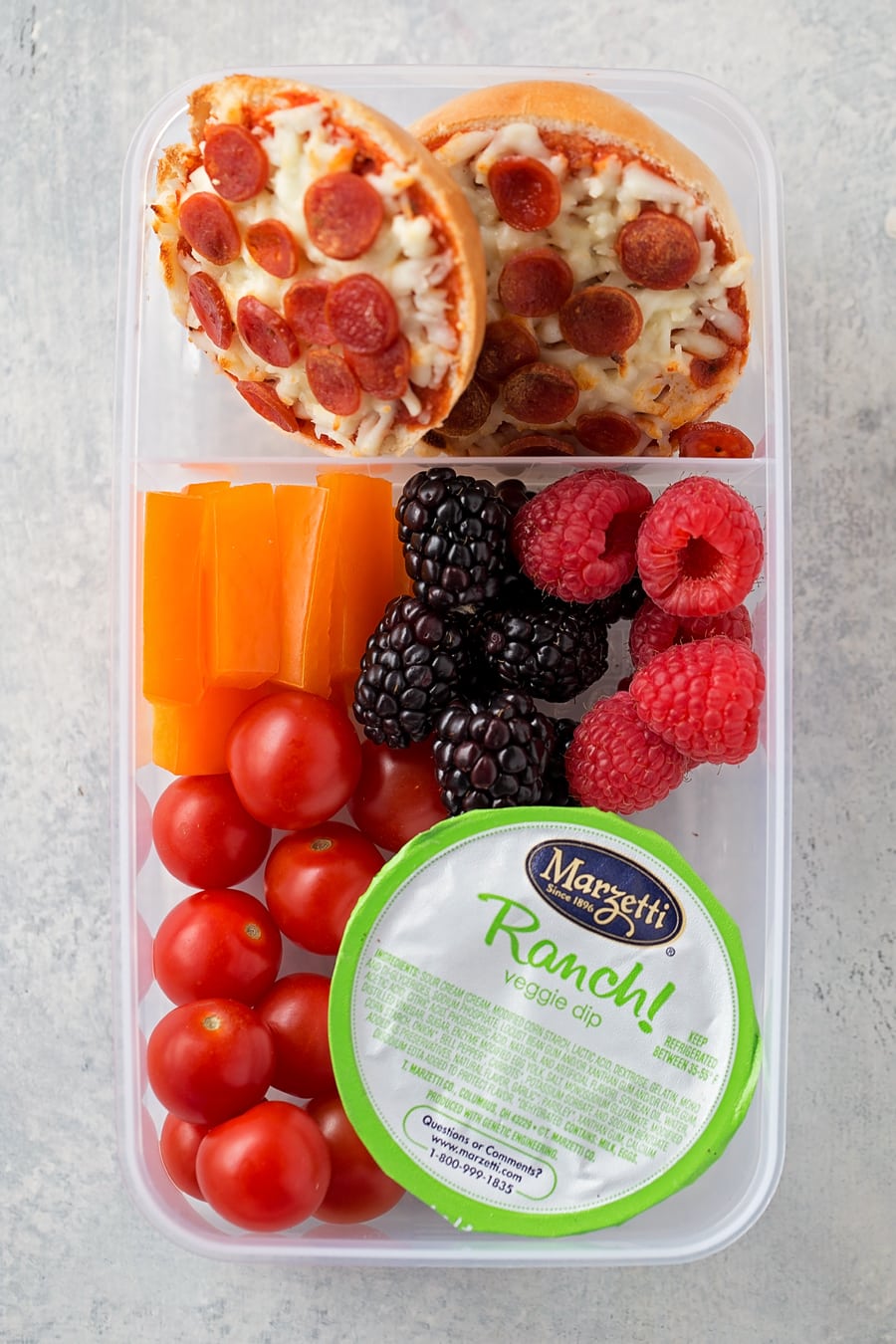 easy lunch box idea with mini pizza bagels, berries, carrots, and tomatoes