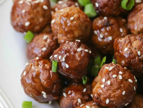 Slow cooker Asian meatballs served on a plate and topped with green onions.