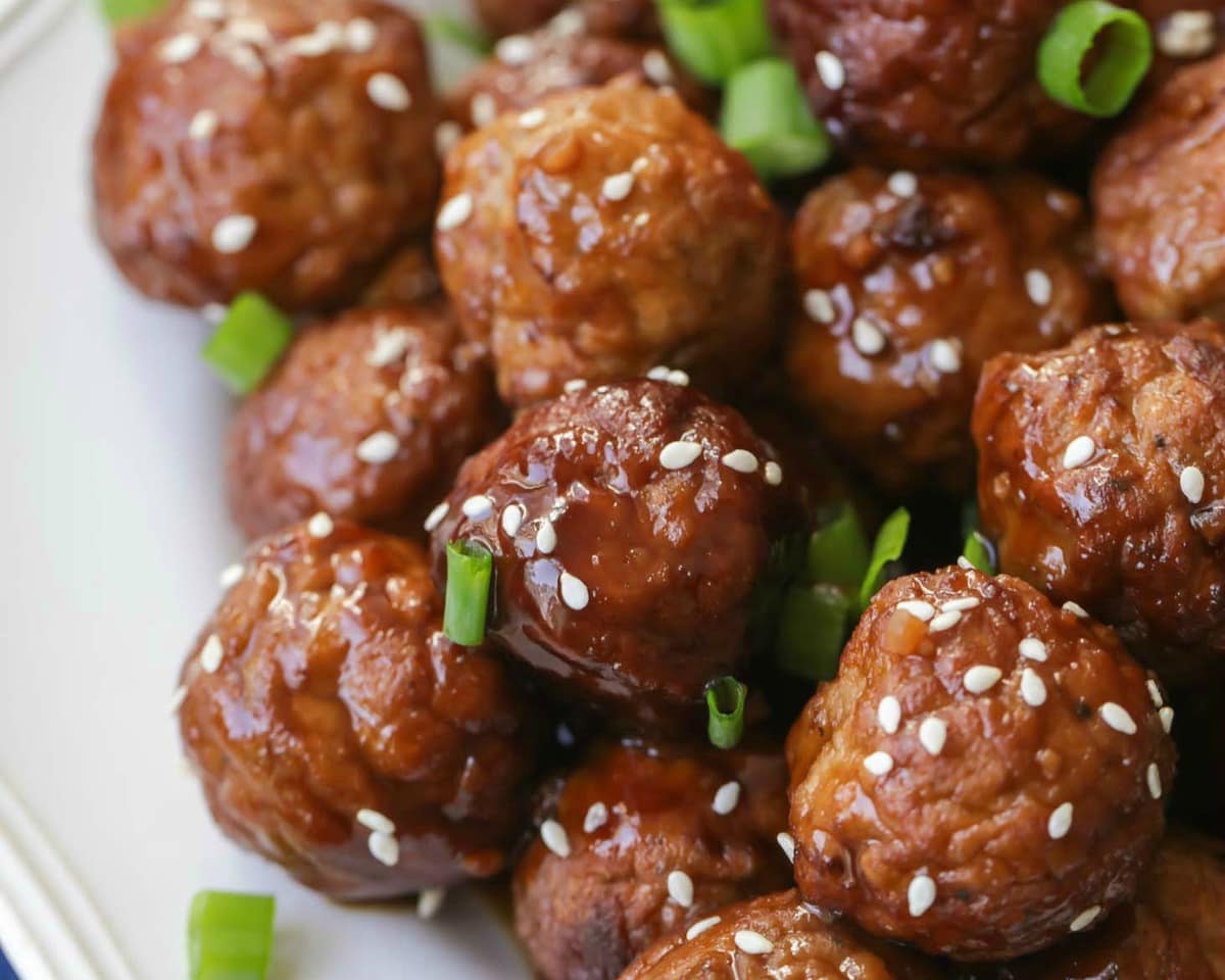 Asian Dinner Recipes - Asian meatballs garnished with sesame seeds and diced green onions on a white plate. 