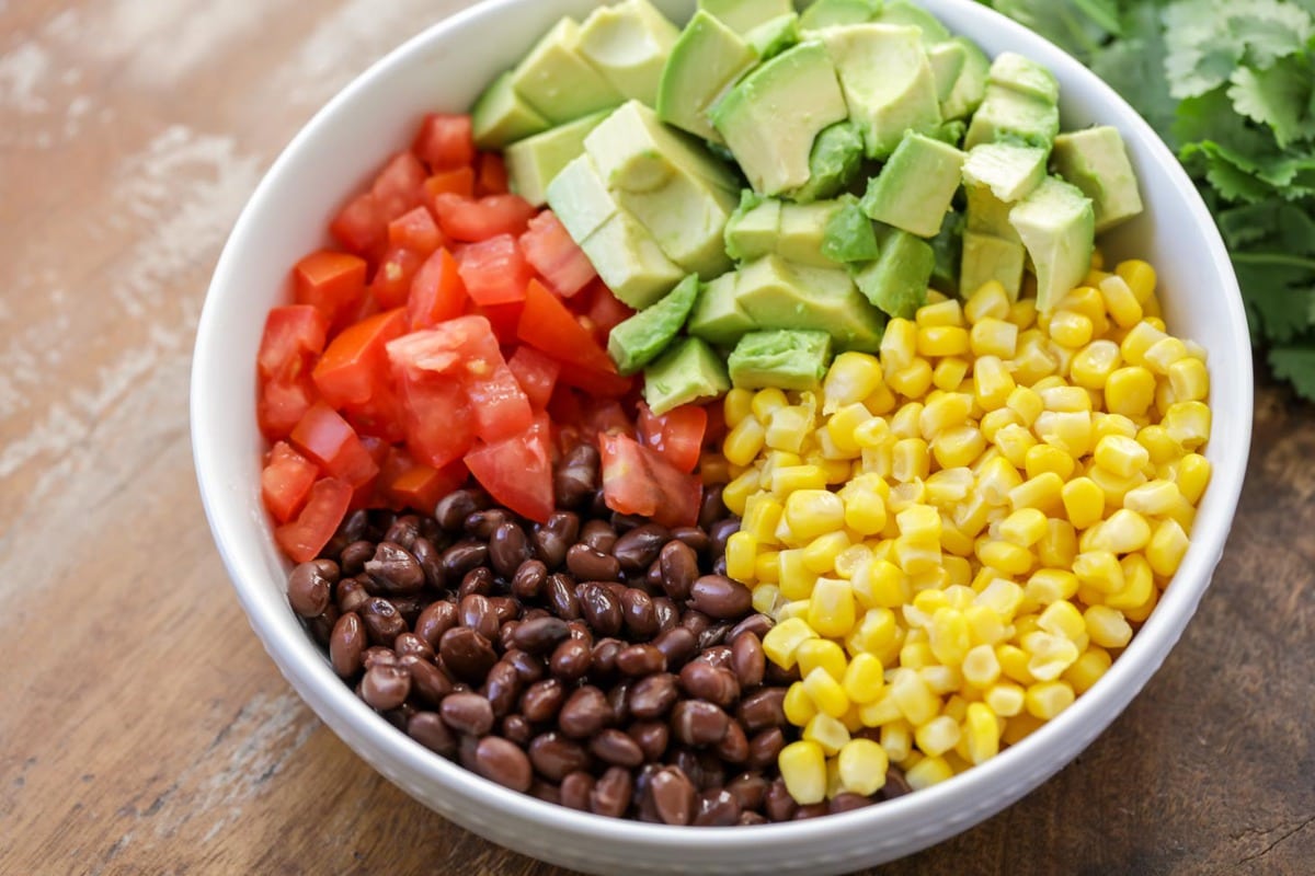 Black beans, corn, tomatoes, and avocado in a white bowl.