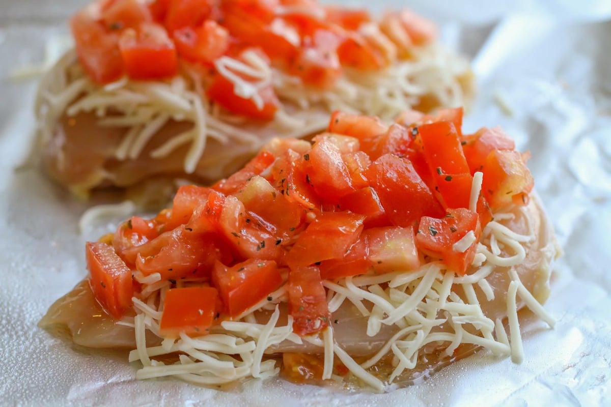 Chicken on foil topped with cheese and tomatoes