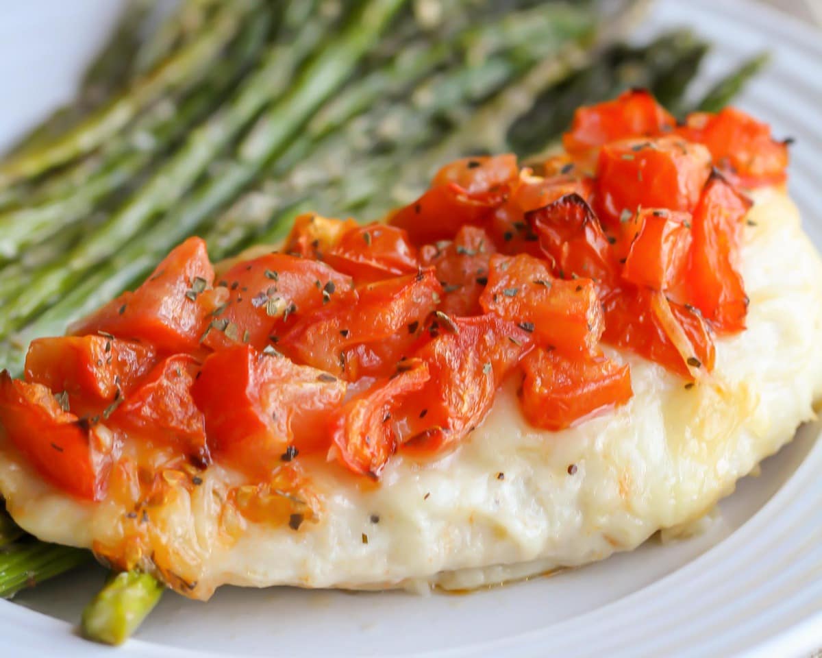 Chicken Bruschetta topped with tomatoes and paired with asparagus on a white plate.