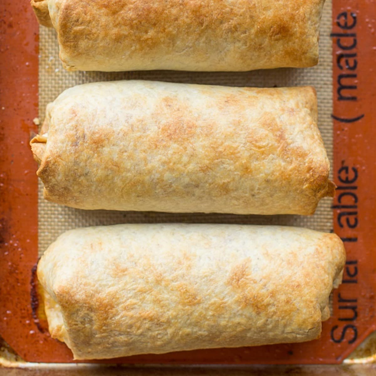 Baked chicken Chimichangas lined up on a silpat.