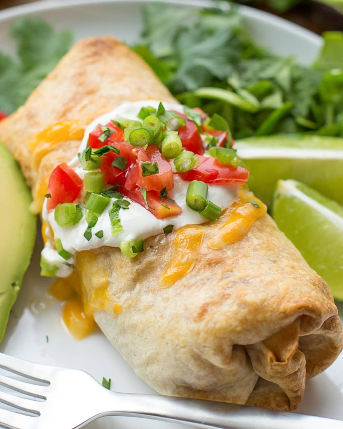 Baked Chimichanga Recipe on plate topped with sour cream and green onions.