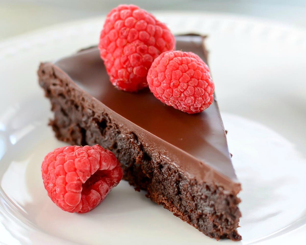 Flourless Chocolate Cake recipe topped with raspberries on a plate.