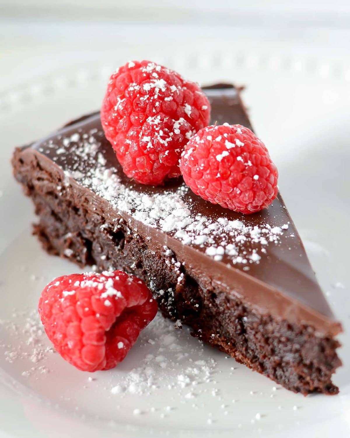 A slice of flourless chocolate cake topped with raspberries and powder sugar.