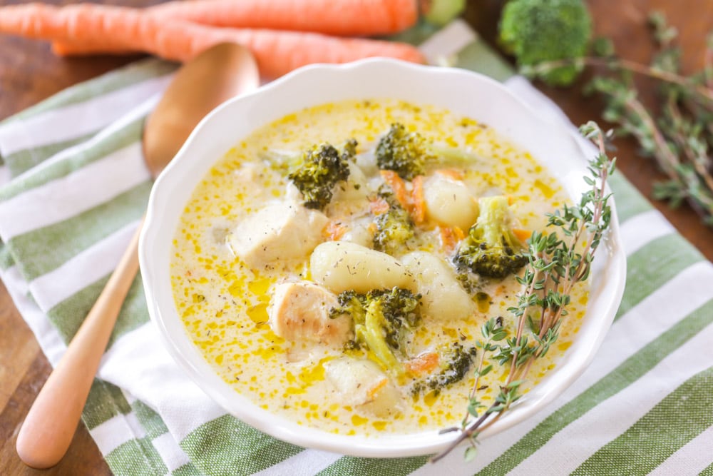 Chicken and gnocchi soup served in a white bowl topped with a sprig of rosemary.