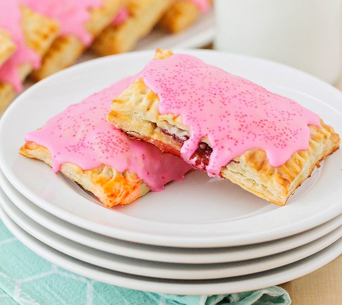 Easy Breakfast Ideas - homemade pop tarts with pink frosting on a stack of white plates. 
