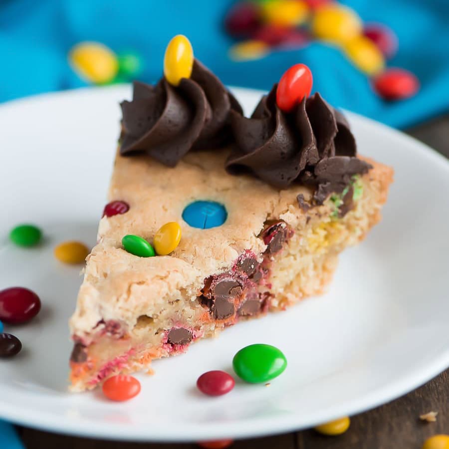 A slice of M&M Cookie Cake on a white plate