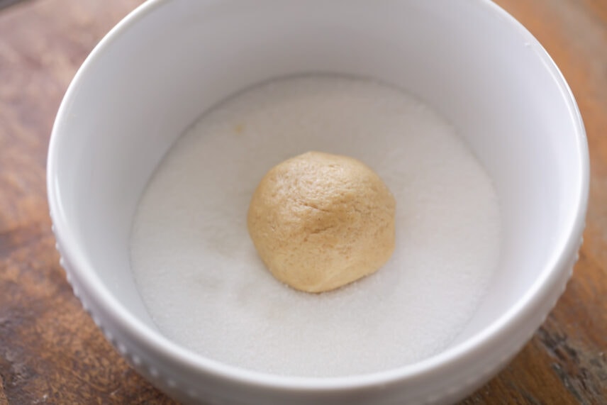Peanut butter cookie dough ball in bowl of sugar