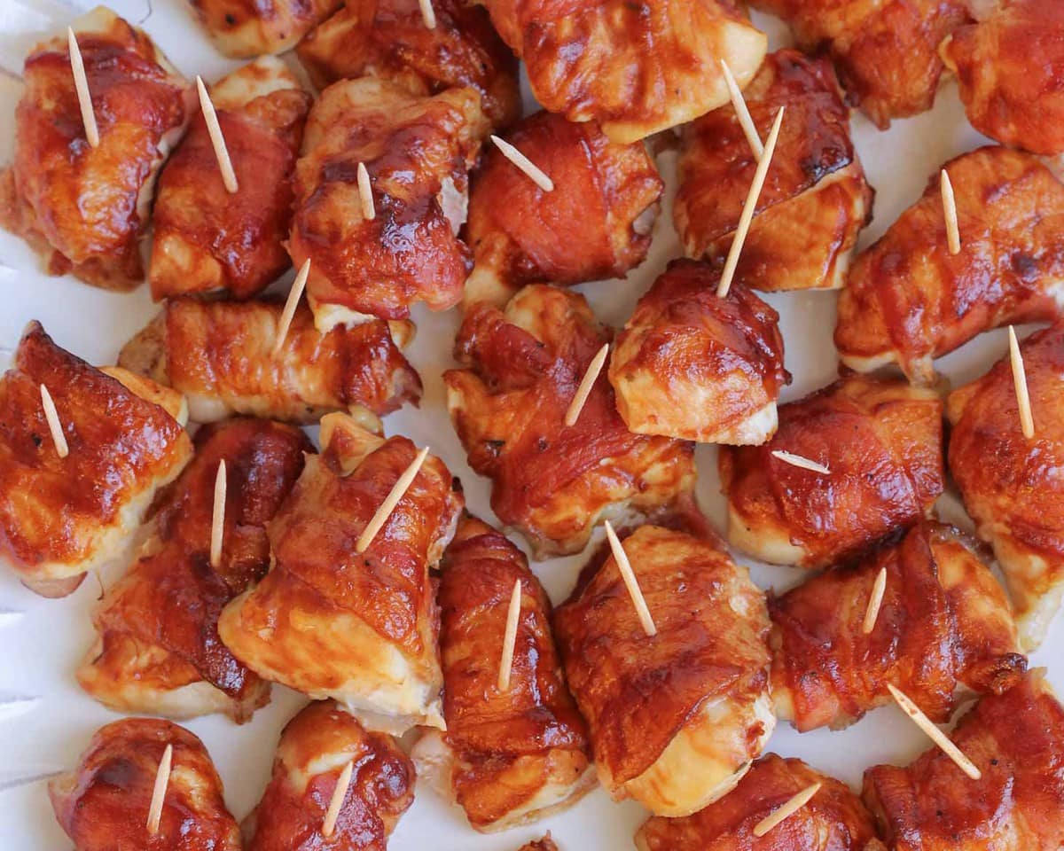 Finger food appetizers - white plate piled with bbq bacon wrapped chicken bites.