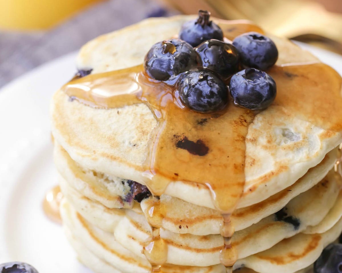 Blueberry Pancakes stacked on a white plate and topped with blueberries.